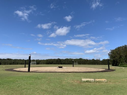 Image of an Aboriginal dance ground with grass in the foreground and blue sky with clouds above.